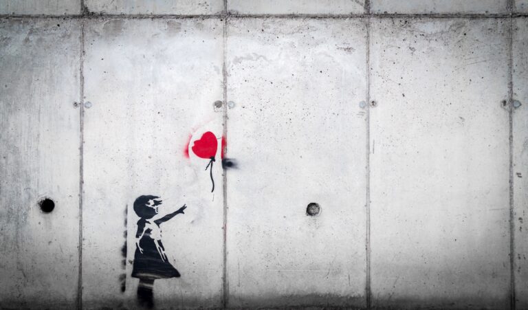 image on concrete wall of small girl with arm outstretched, reaching toward a red heart-shaped ballon that has slipped from her grasp